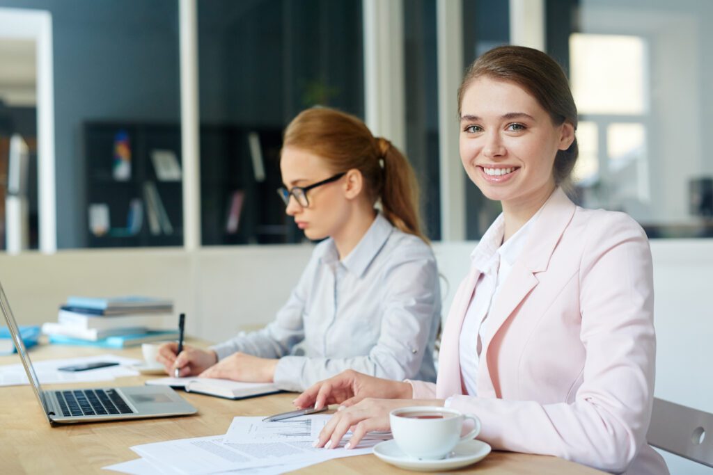 Two women working at a desk, smiling.